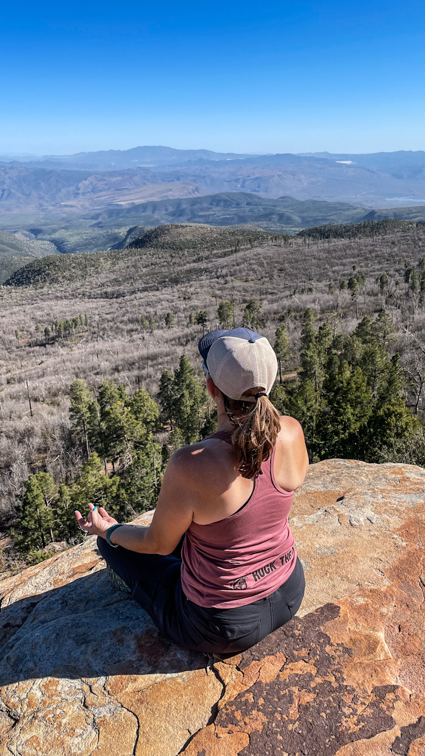 woman sitting on the edge of a cliff overlooking a valley